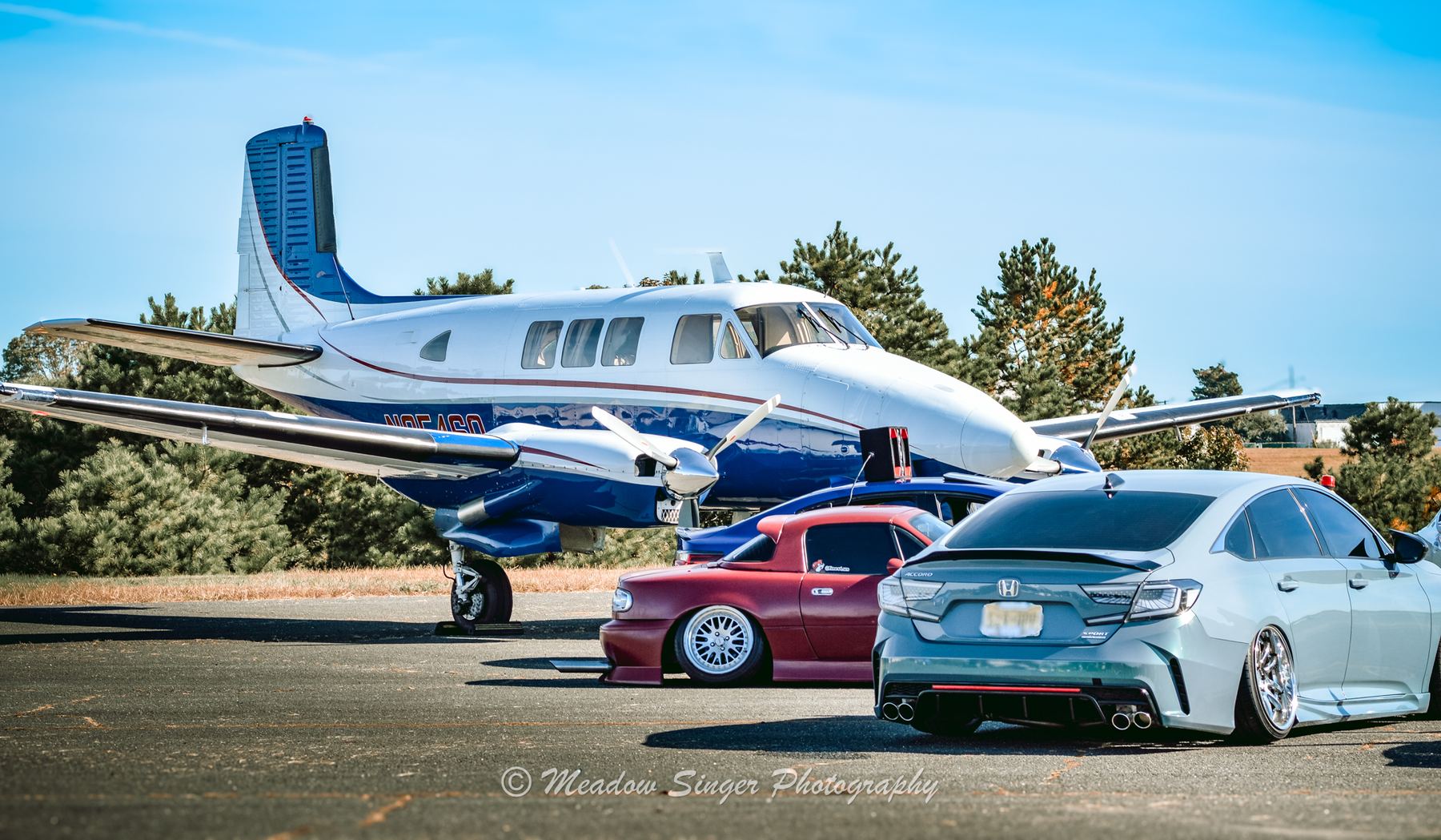 Tuned cars parked beside a small propeller plane at an airfield show