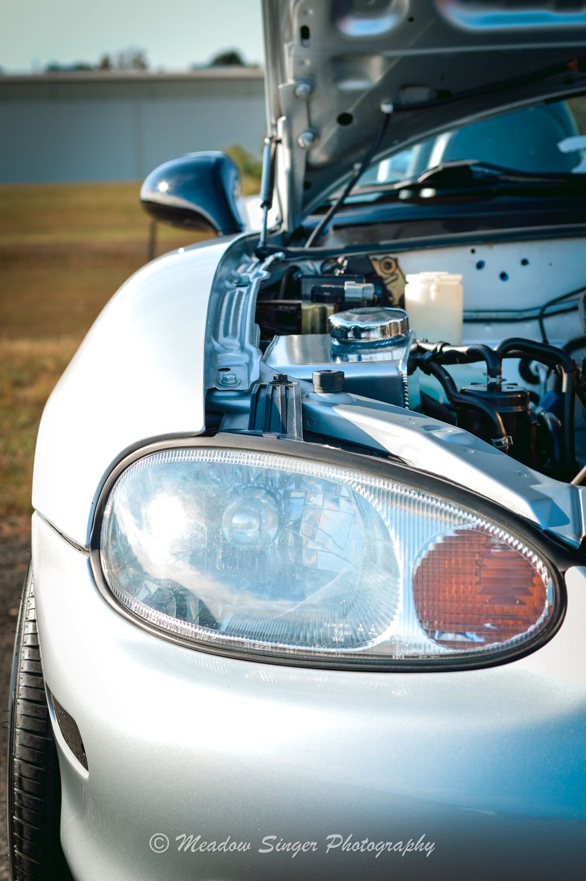 The headlight of a white roadster with its hood up