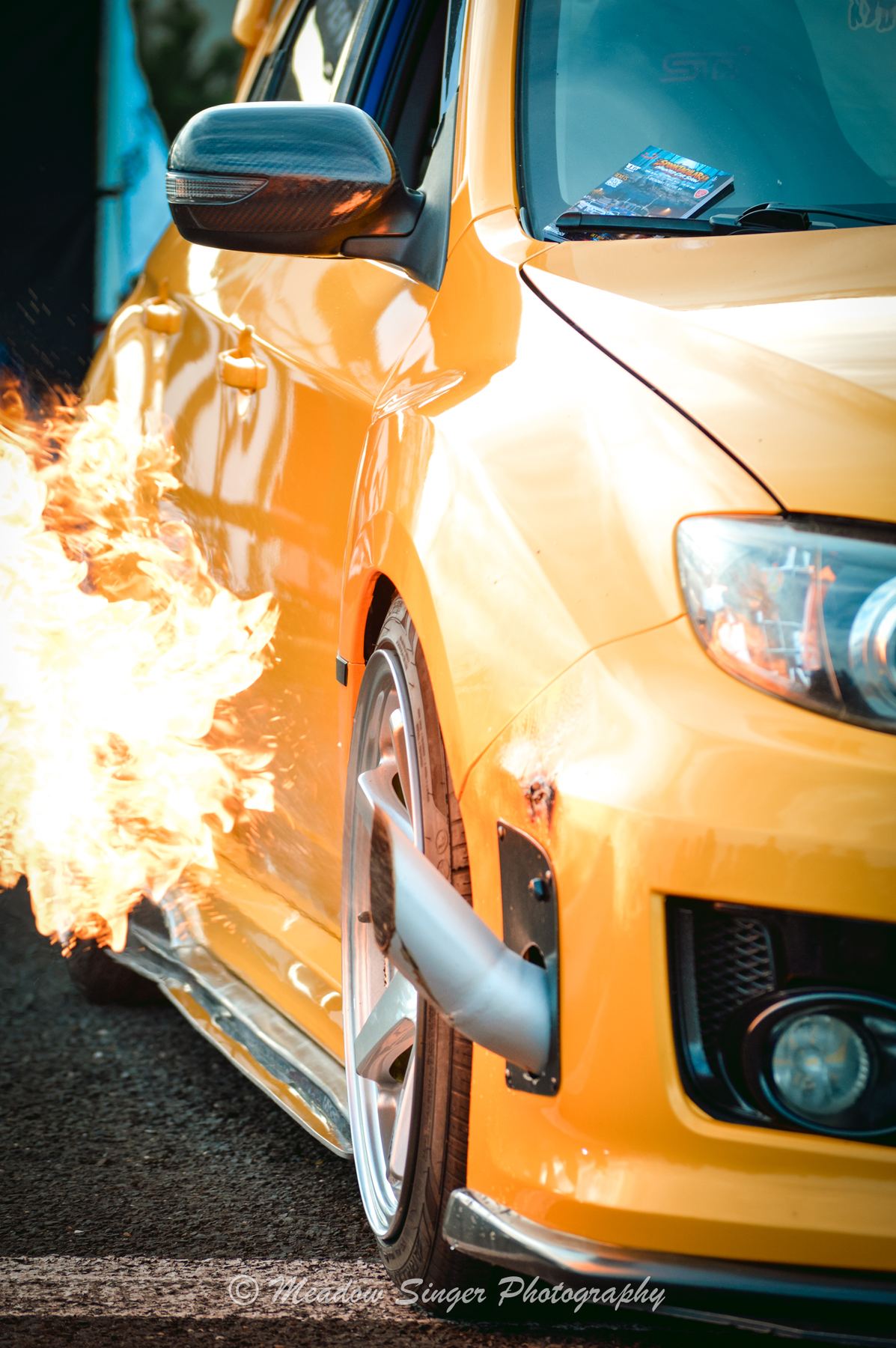A yellow hatchback with flames bursting from its side exhaust